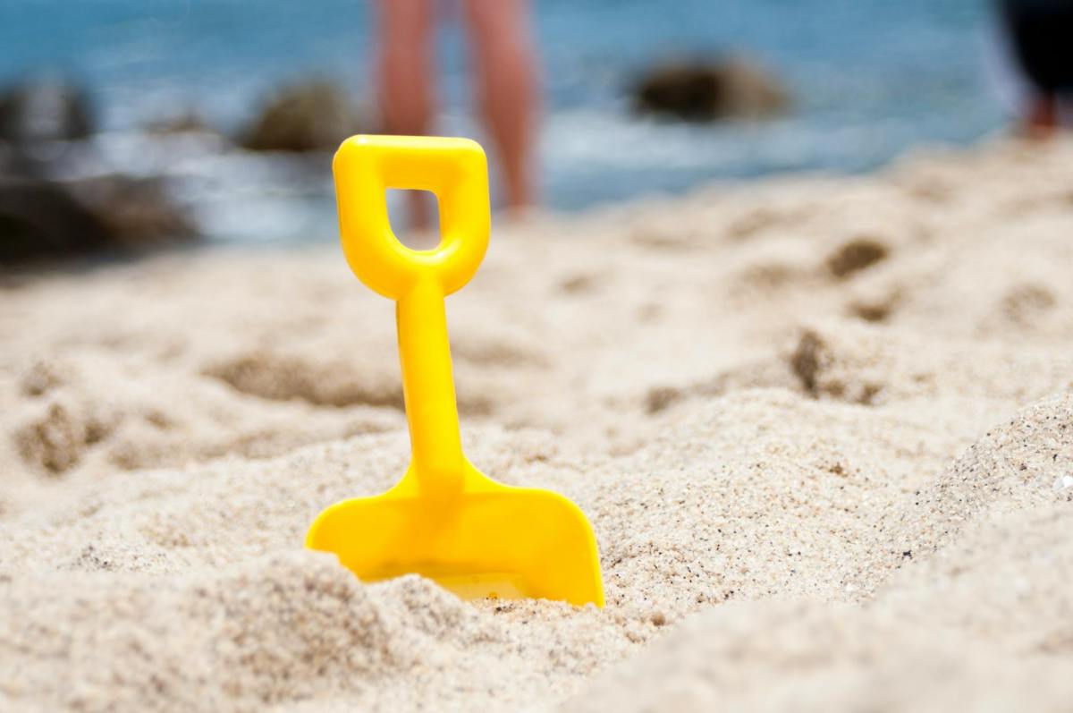 Decorative - yellow shovel half buried on sand near the sea